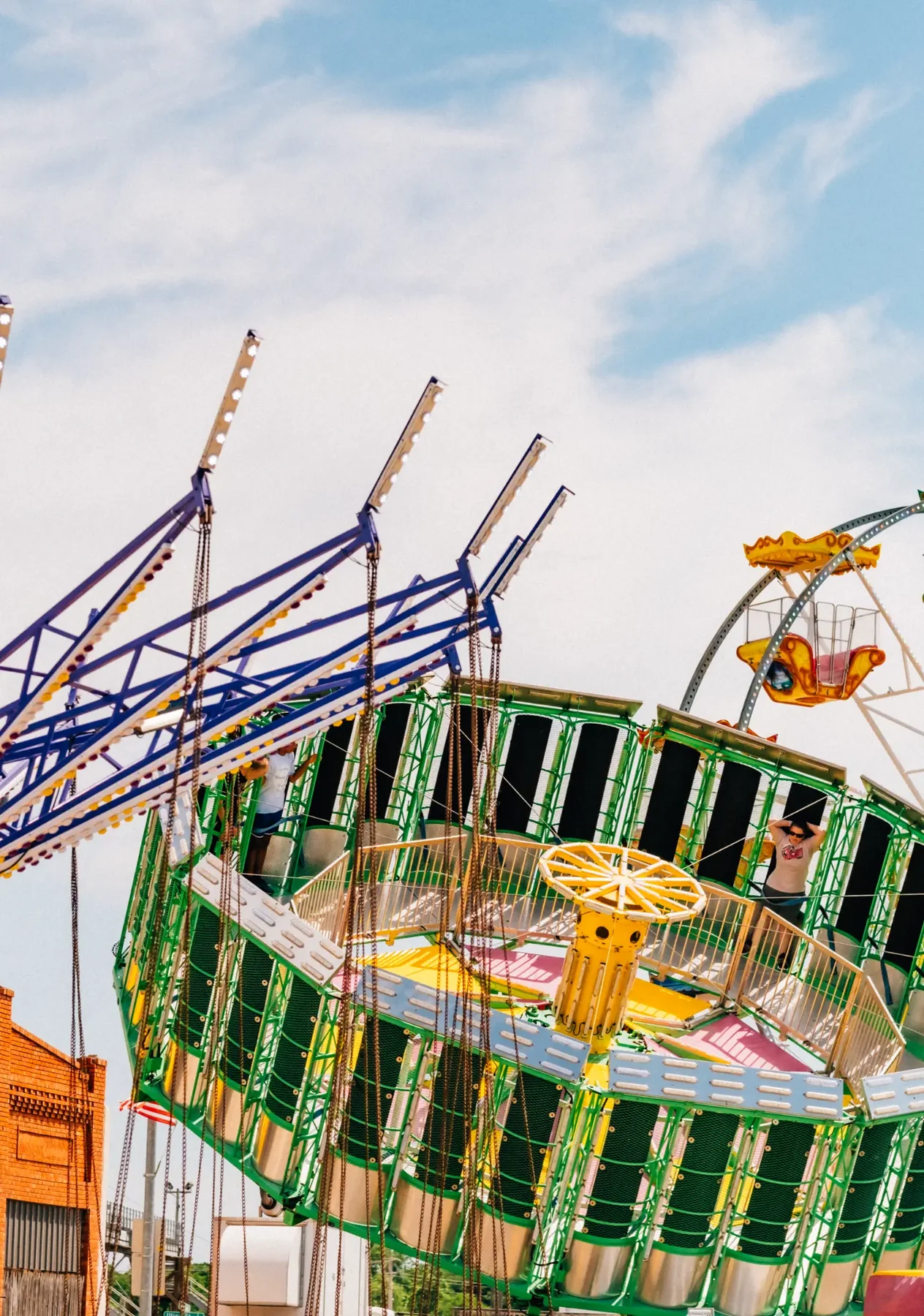 Swing ride and carnival attractions under a cloudy sky.