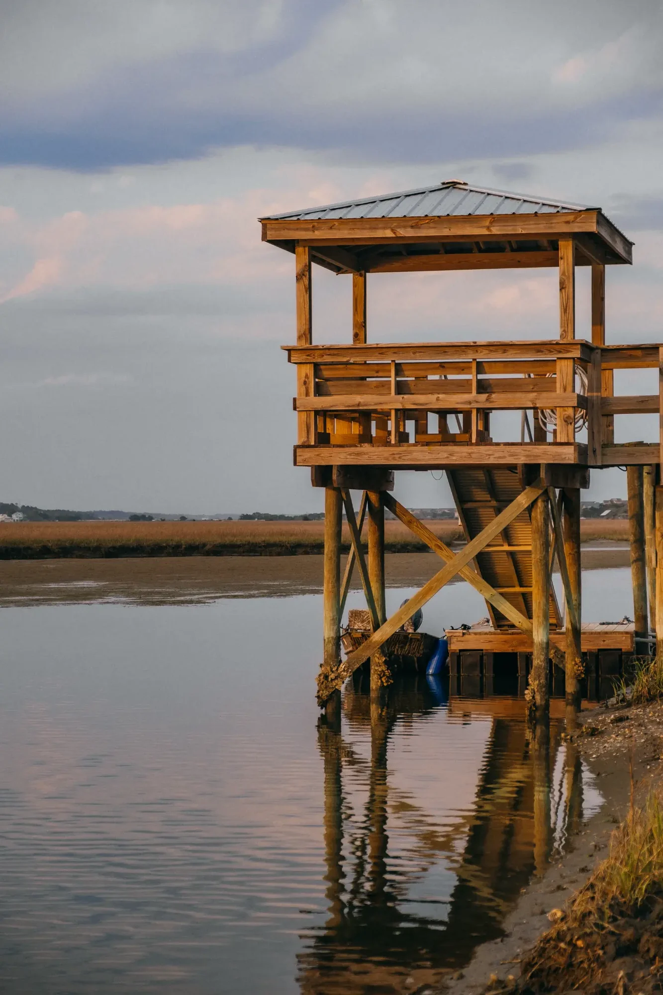 Wooden elevated observation platform on stilts over calm water with warm sunset reflection.