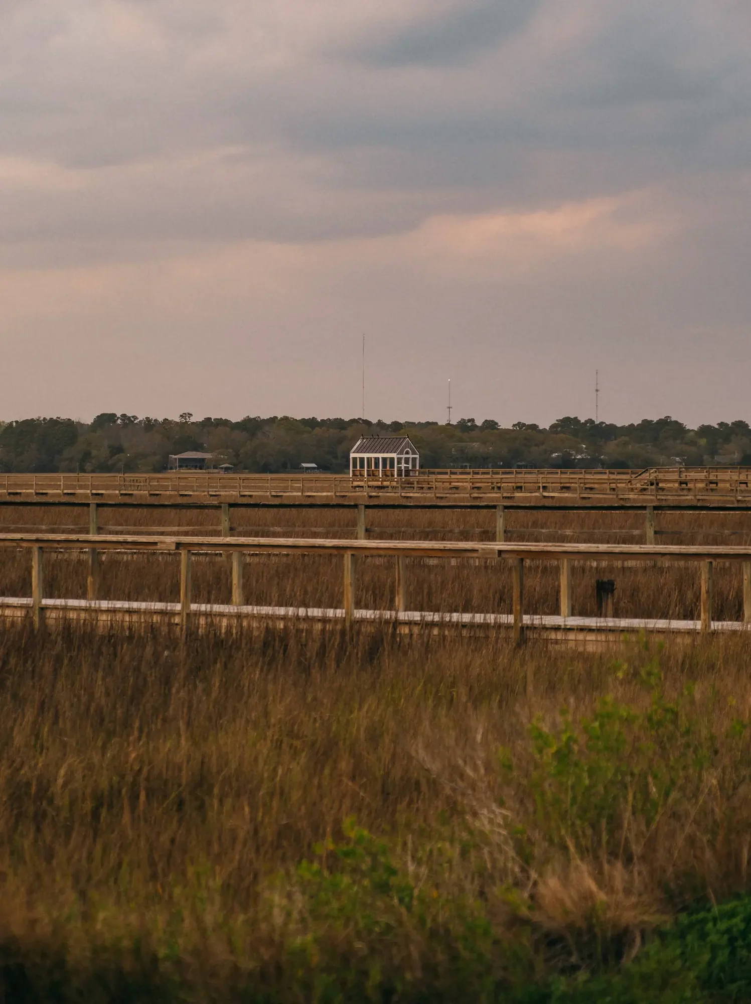 Marsh with layered wooden boardwalks leading to a small white pavilion under pastel sky.