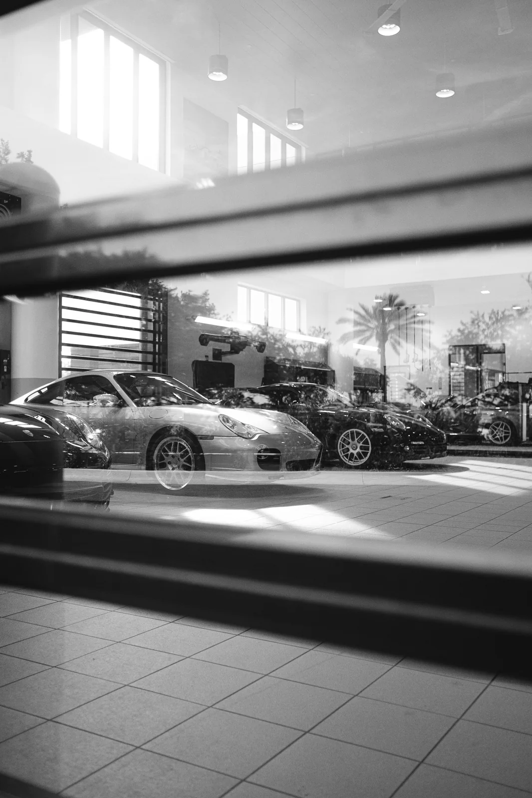 Black-and-white Porsche sports car reflected through showroom glass.