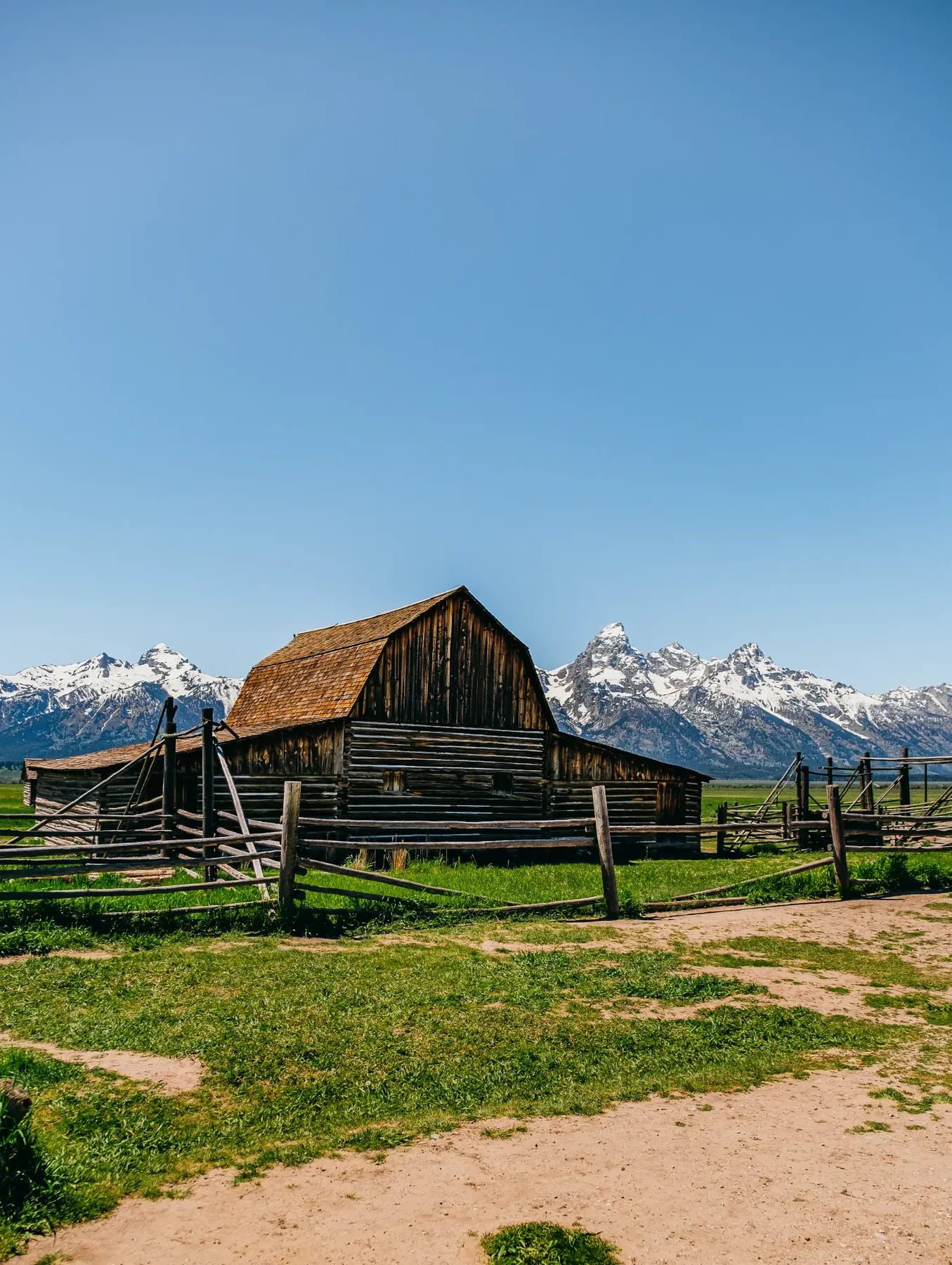 Historic wooden barn and split-rail fence with the Tetons in the distance.