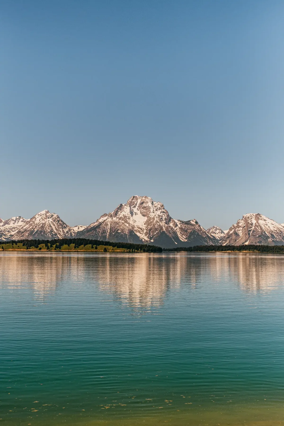 Grand Teton range reflected across still blue lake water.