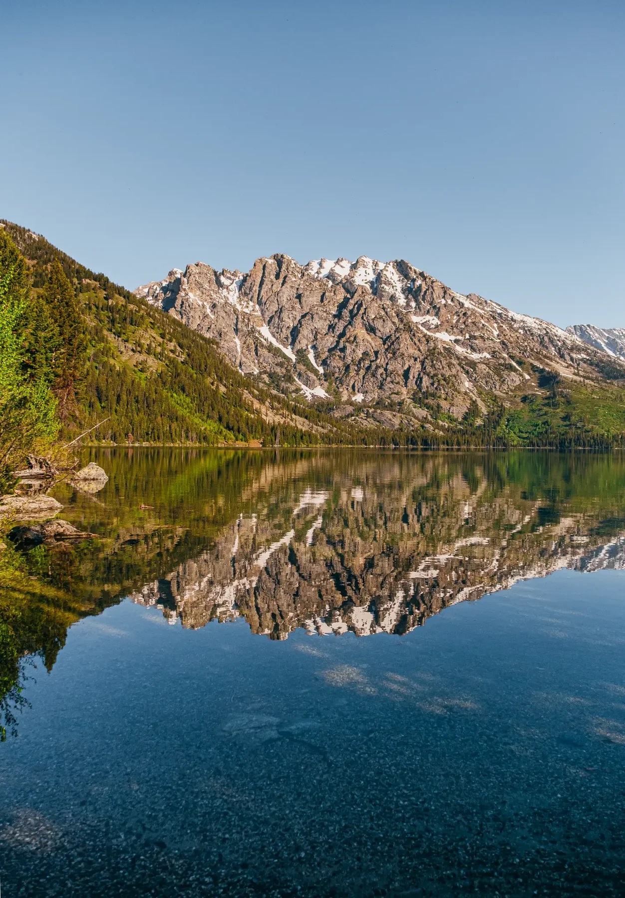 Mountain peak reflected in a clear alpine lake beneath a soft blue sky.