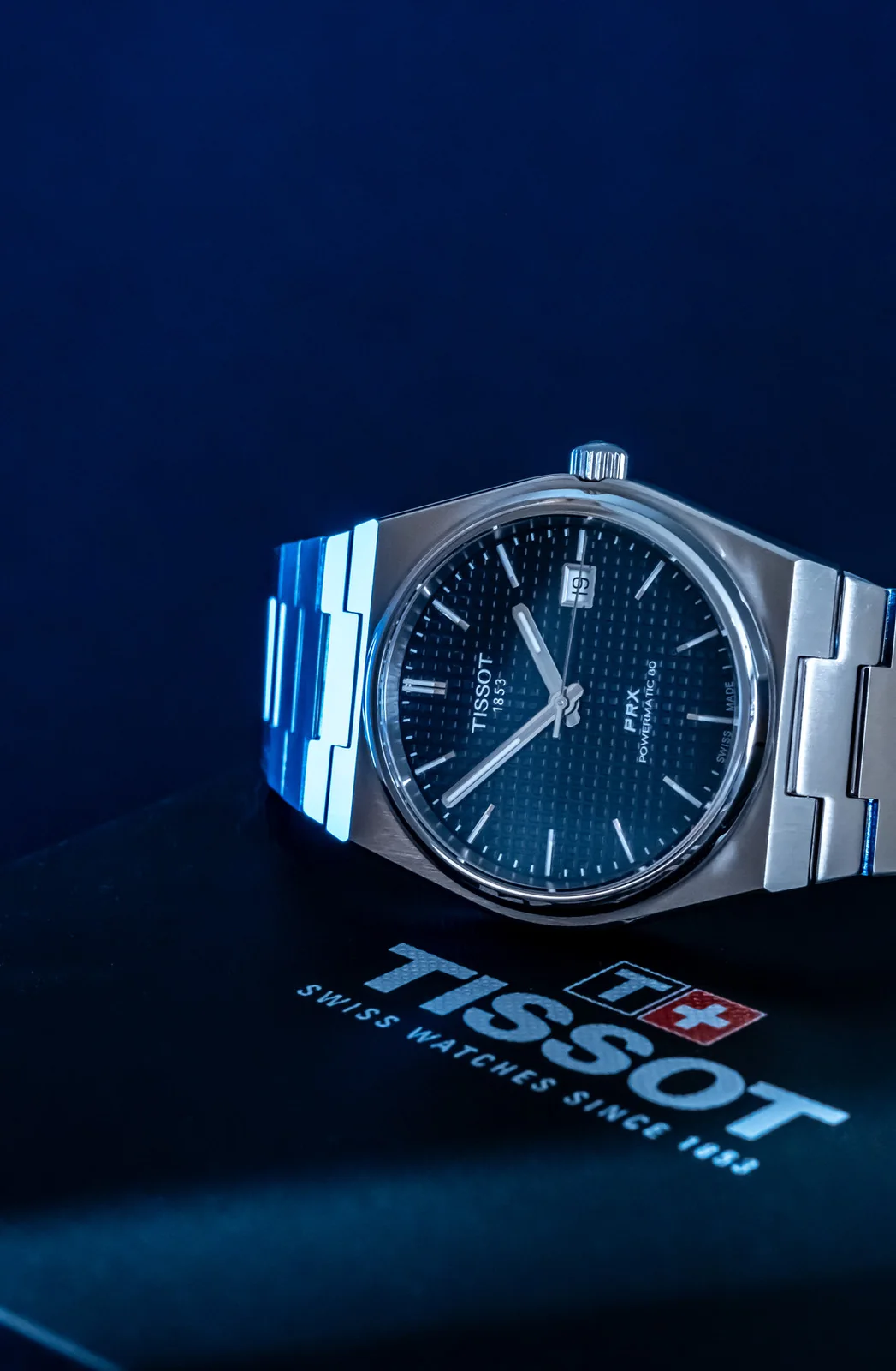 Close view of a Tissot PRX watch on a deep blue surface with Tissot lettering.