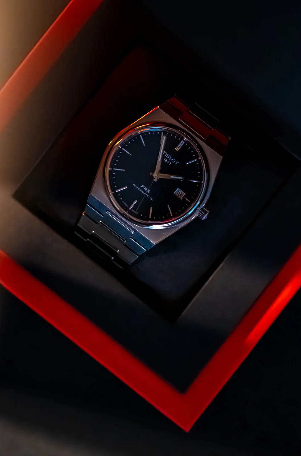 Tissot PRX watch resting in a dark display box edged with red light.