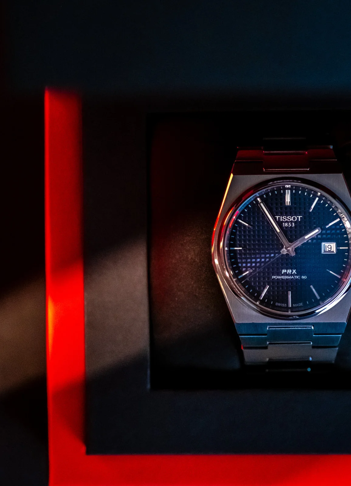 Tissot PRX watch upright in a black presentation box with red accent lighting.
