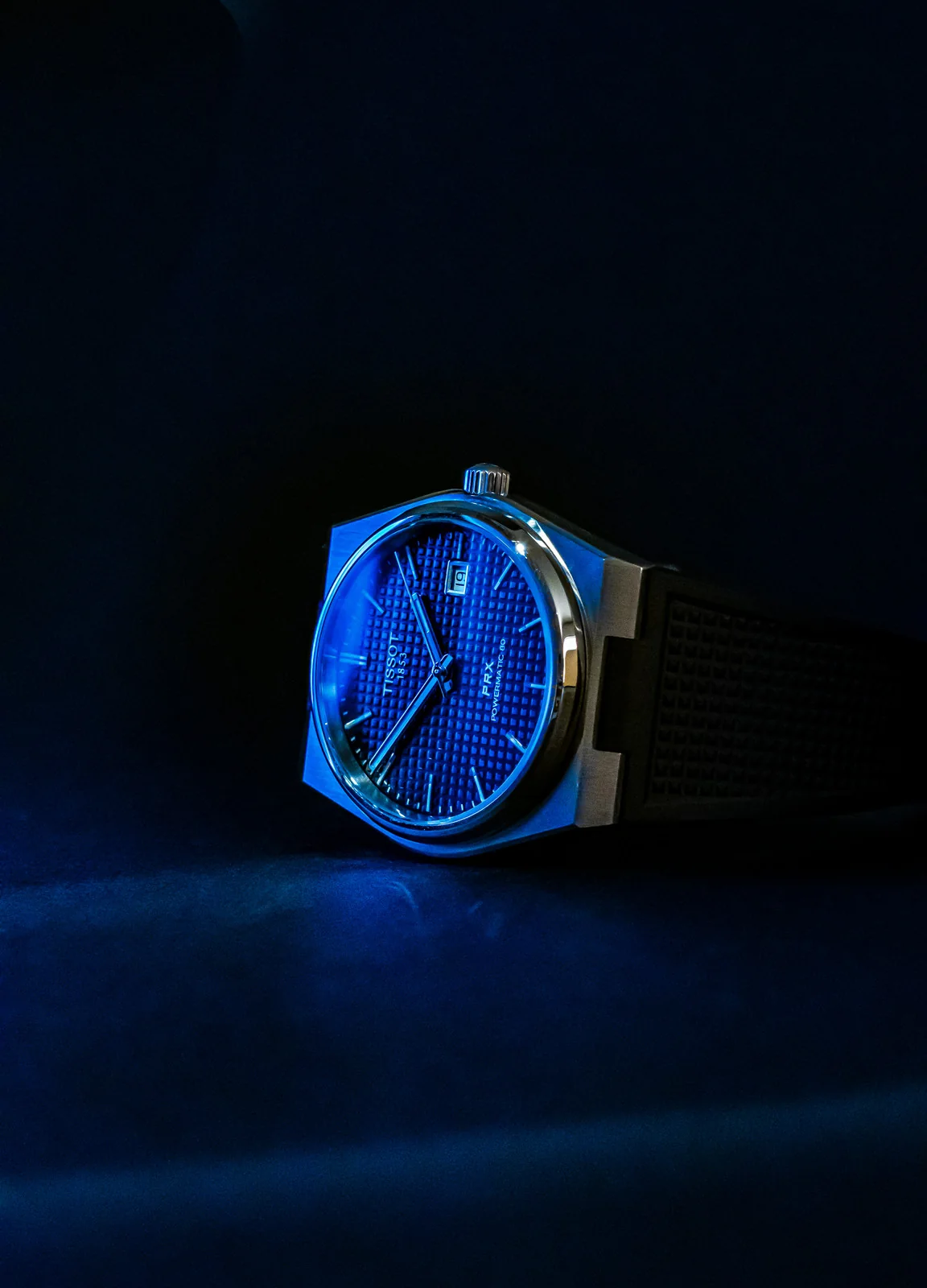 Tissot PRX watch angled on a dark blue surface with a patterned dial.