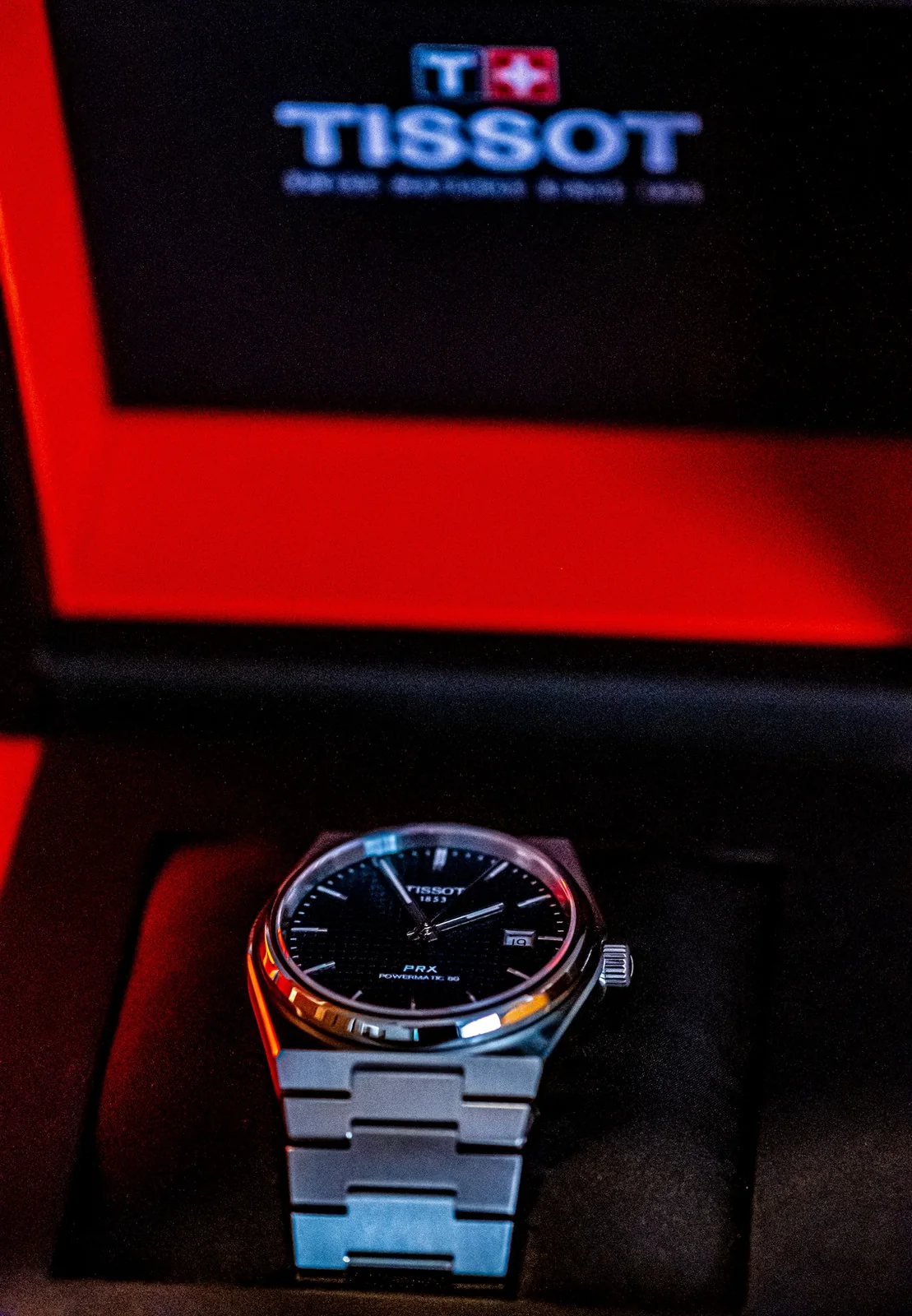 Tissot PRX watch in a dark presentation box framed by red light.